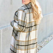 Woman wearing a plaid coat standing against a light-colored wall.