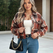 Person wearing a plaid shirt, white top, blue jeans, and holding a black handbag.