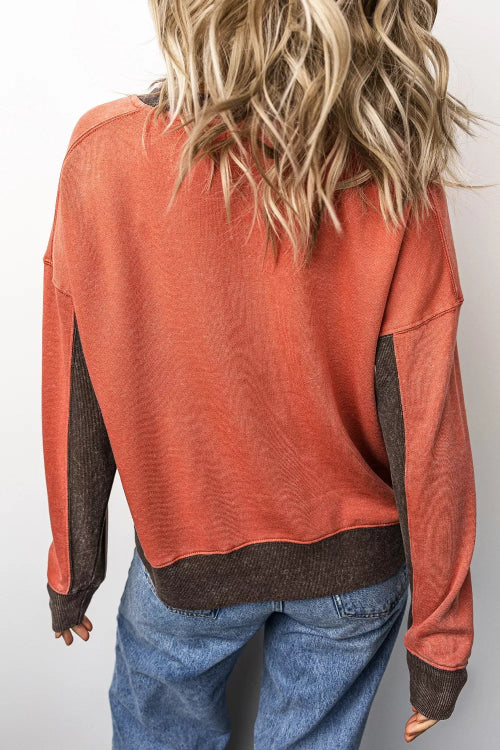 A person shown from the back wearing a long-sleeve textured sweatshirt in burnt orange with dark brown contrast panels 