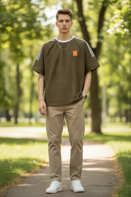 Brown t-shirt with white stripes on sleeves and a small patch, worn by a person.