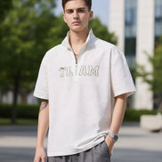 Person wearing a light gray short-sleeve shirt with 'TEAM' text on a plain background