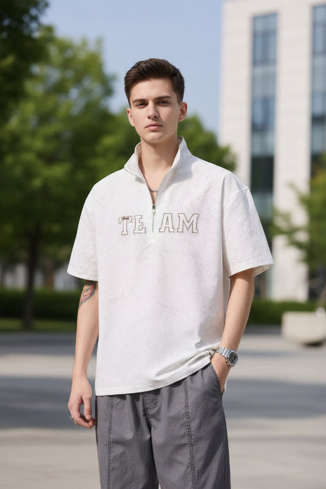 Person wearing a light gray short-sleeve shirt with 'TEAM' text on a plain background