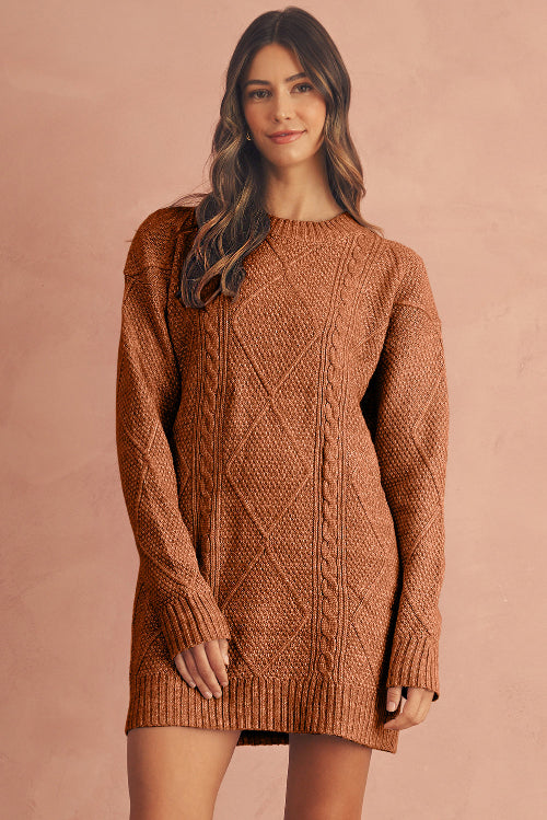 Woman wearing a brown cable knit sweater dress against a pink background