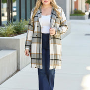Woman wearing a plaid coat standing against a light-colored wall.