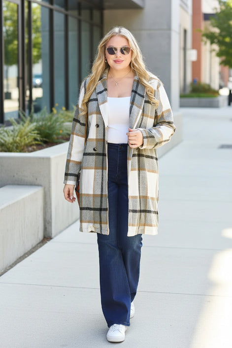 Woman wearing a plaid coat standing against a light-colored wall.