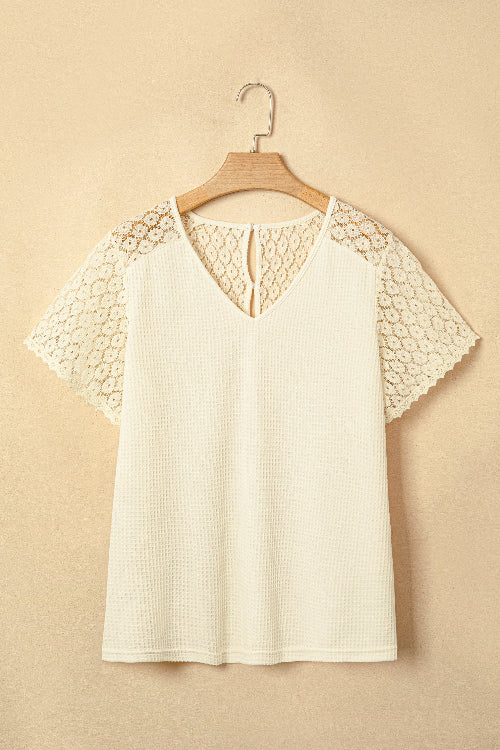 White blouse with lace sleeves on a wooden hanger against a beige background