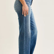 Side view of women’s Judy Blue straight-leg jeans showing faded blue denim and stitched hems, worn with a blue striped top and brown slide sandals.