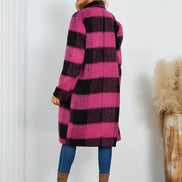 Woman wearing a pink and black checkered coat with blue pants and brown boots, standing against a white wall.