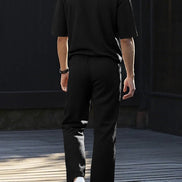 A man viewed from behind wearing a black short-sleeve polo shirt and black trousers, 