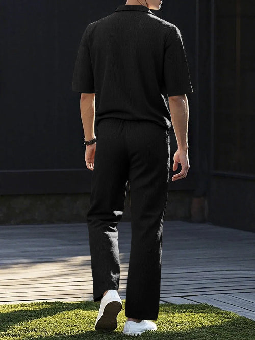 A man viewed from behind wearing a black short-sleeve polo shirt and black trousers, 