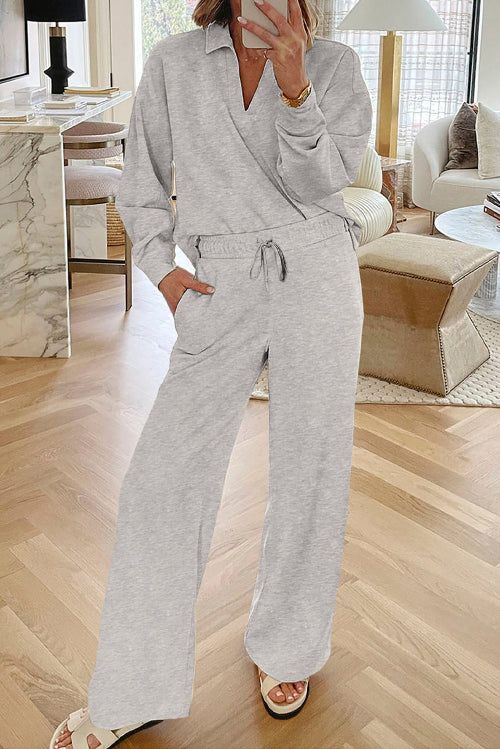 A woman wearing a light gray heathered two-piece loungewear set consisting of a long-sleeve collared top and matching wide-leg pants, 