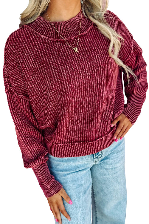 A woman wearing a ribbed knit long-sleeve sweater in a deep burgundy red, paired with light blue jeans, 