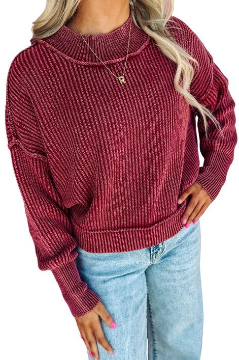 A woman wearing a ribbed knit long-sleeve sweater in a deep burgundy red, paired with light blue jeans, 